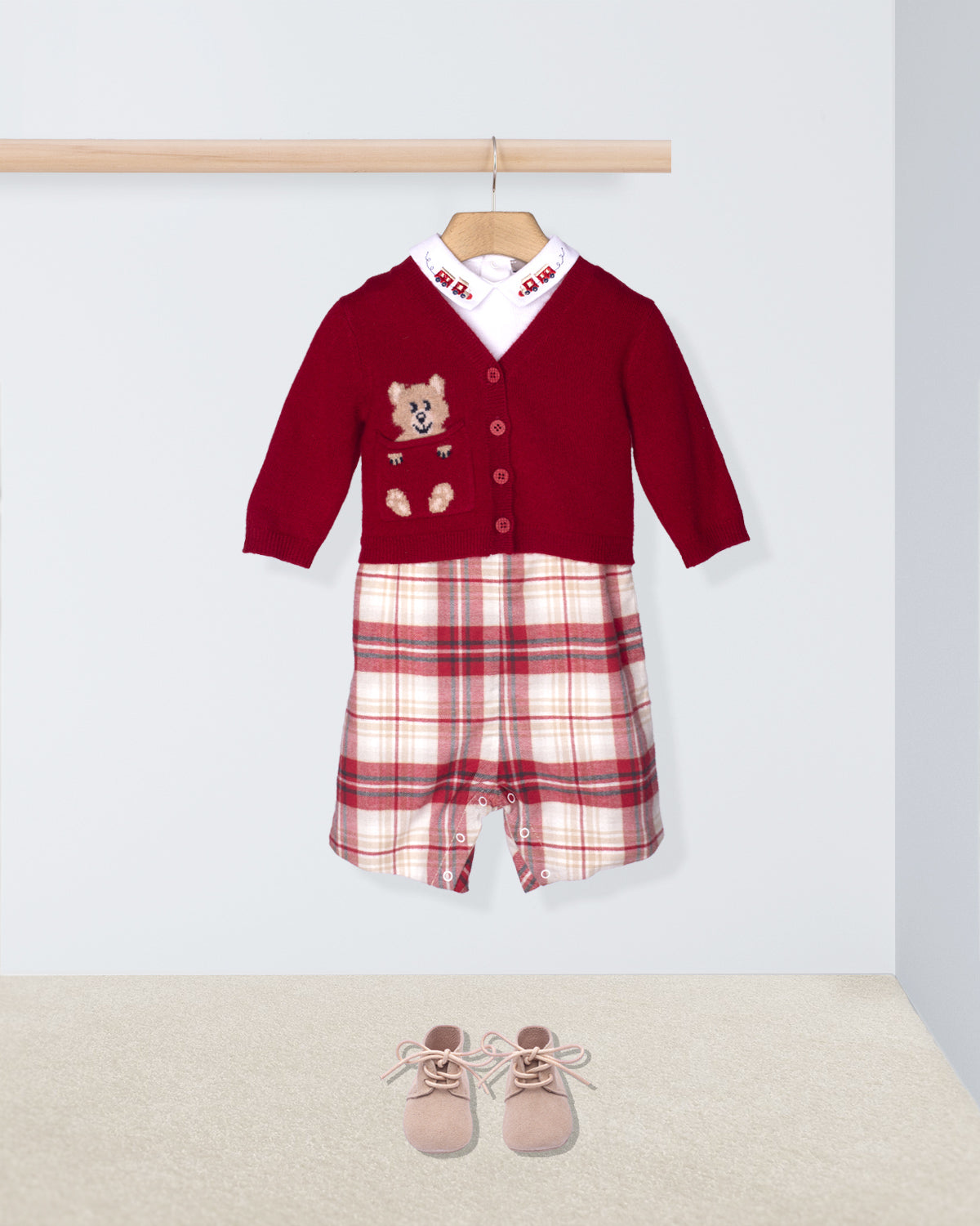 Children's outfit with red sweater and plaid pants on a hanger, accompanied by pink shoes on the floor.