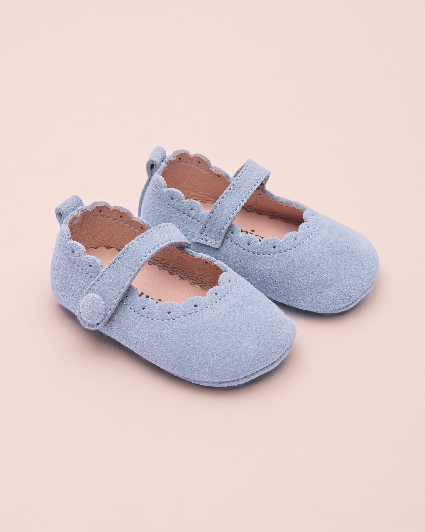 Pair of light blue children's crib shoes on a beige background