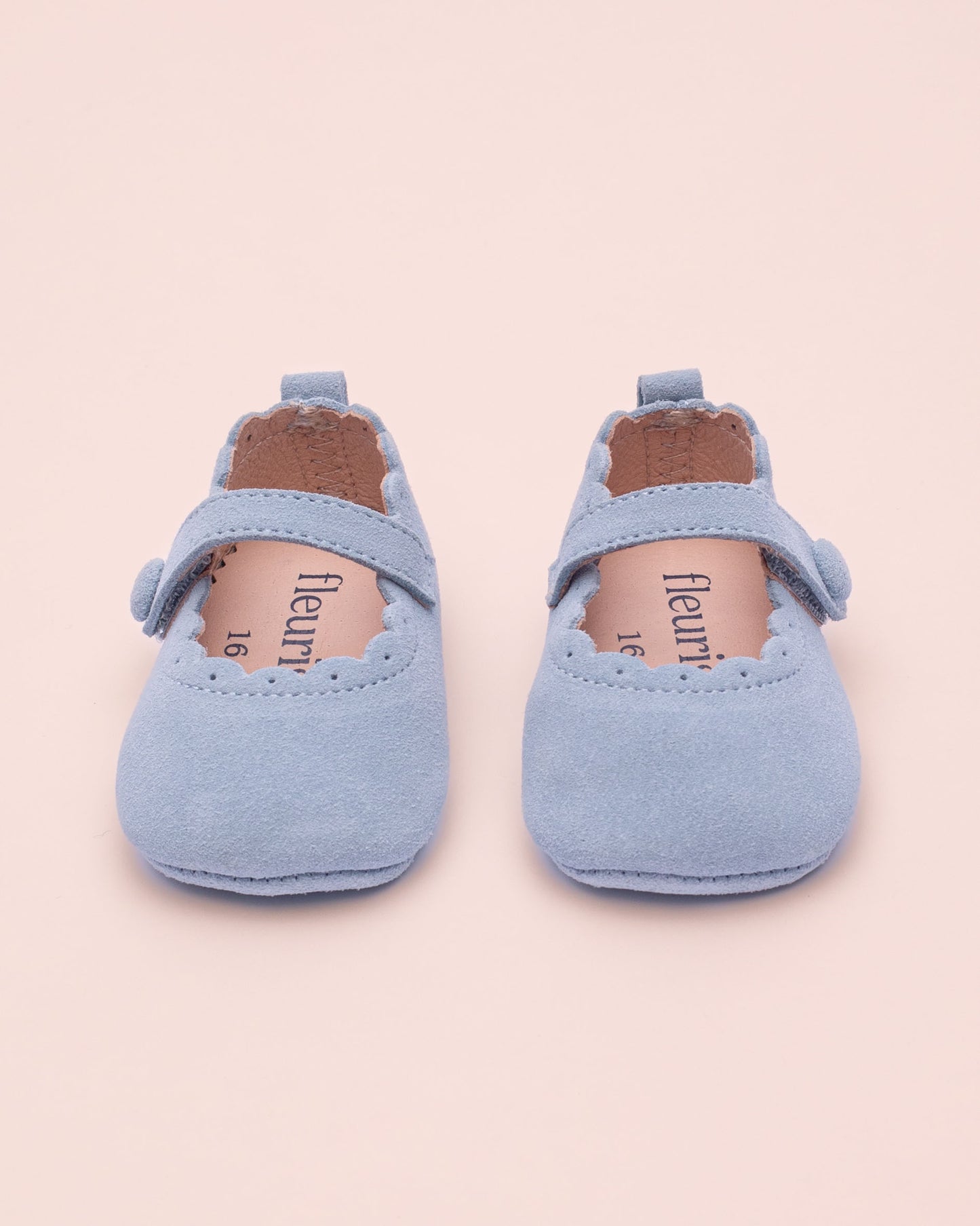 Pair of light blue baby shoes on a beige background