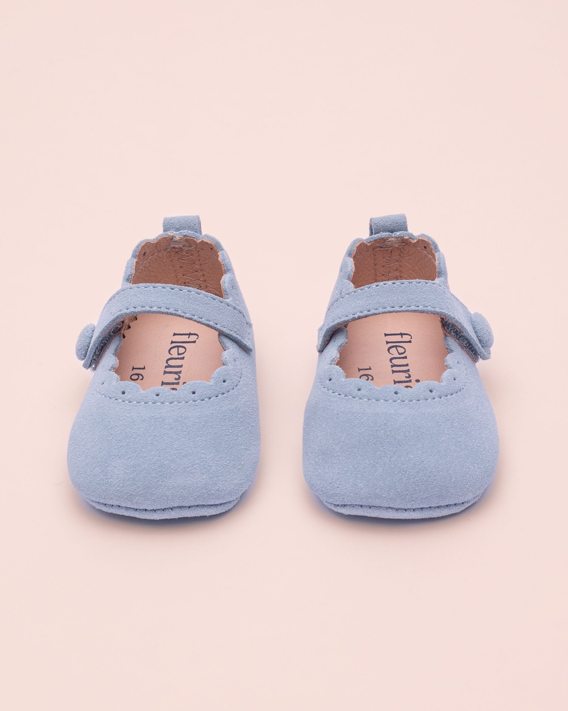 Pair of light blue baby shoes on a beige background
