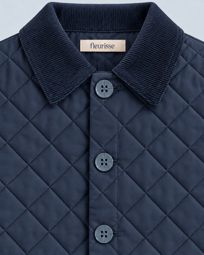 Close-up of a navy quilted collared jacket with a ribbed corduroy-style collar and matching buttons, showing a small Fleurisse label at the inner neck.
