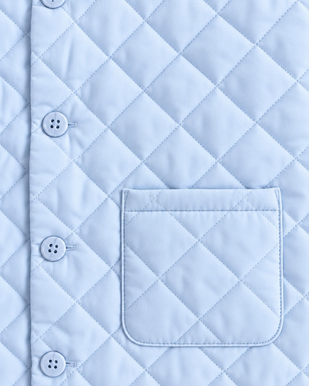 Close-up of a light blue quilted garment with a diamond stitching pattern, a vertical button placket with white buttons, and a matching pocket.