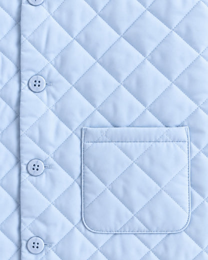 Close-up of a light blue quilted garment with a diamond stitching pattern, a vertical button placket with white buttons, and a matching pocket.