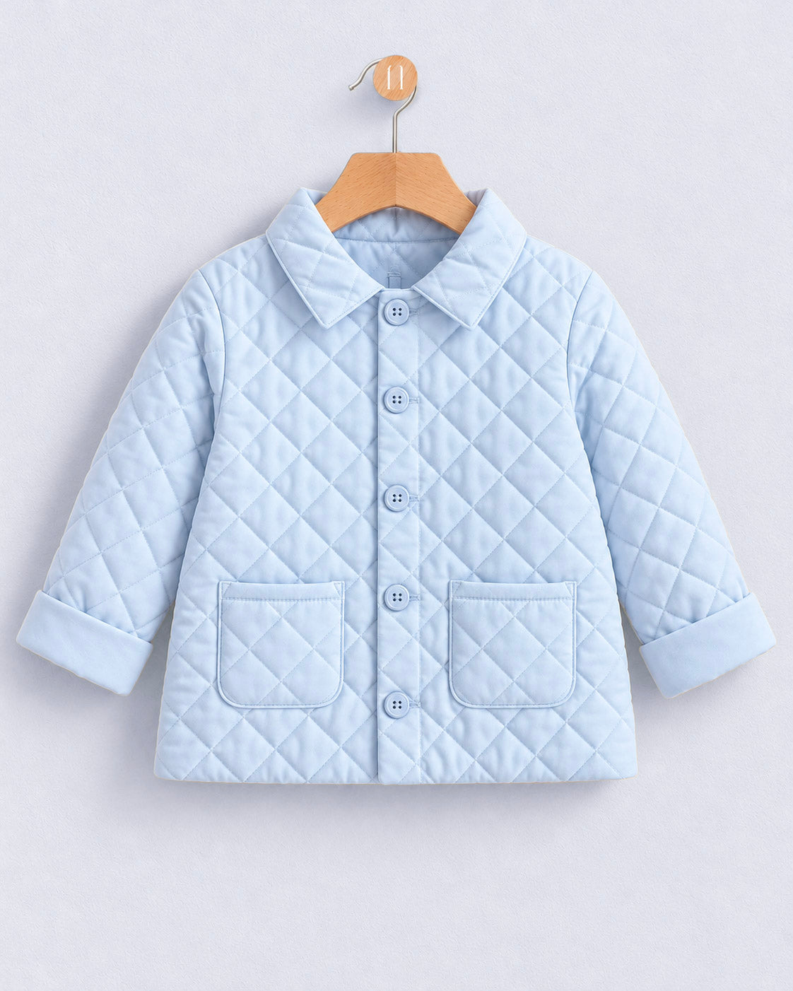 A light blue quilted baby jacket with a pointed collar, button front, and two front patch pockets, hanging on a wooden hanger against a light gray background.