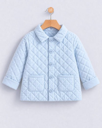 A light blue quilted baby jacket with a pointed collar, button front, and two front patch pockets, hanging on a wooden hanger against a light gray background.