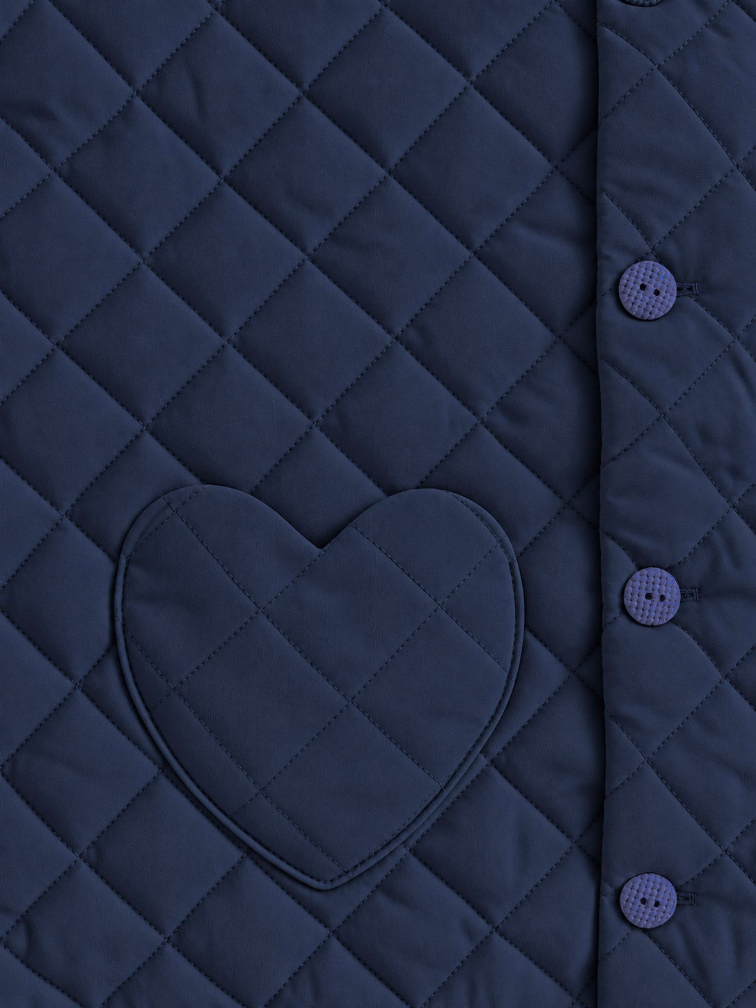Close-up of a quilted navy jacket or vest with a heart-shaped patch pocket and matching buttons on the side.