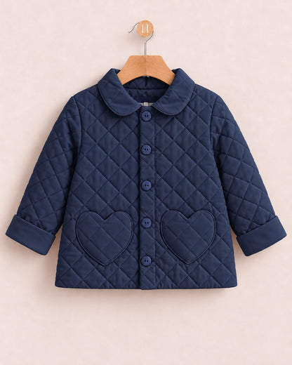 A navy blue quilted baby jacket with a Peter Pan collar, button front, and two heart-shaped pockets, hanging on a wooden hanger against a light beige background.
