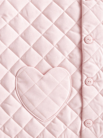 Close-up of a light pink quilted fabric with a diamond pattern, a heart-shaped patch pocket, and a buttoned edge.