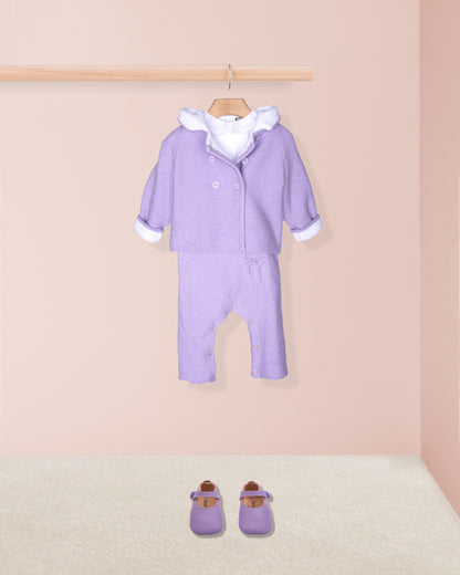 Purple baby outfit with white trim on a wooden hanger against a pink wall.