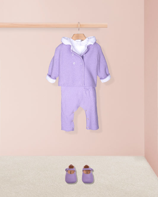 Purple baby outfit with white trim on a wooden hanger against a pink wall.