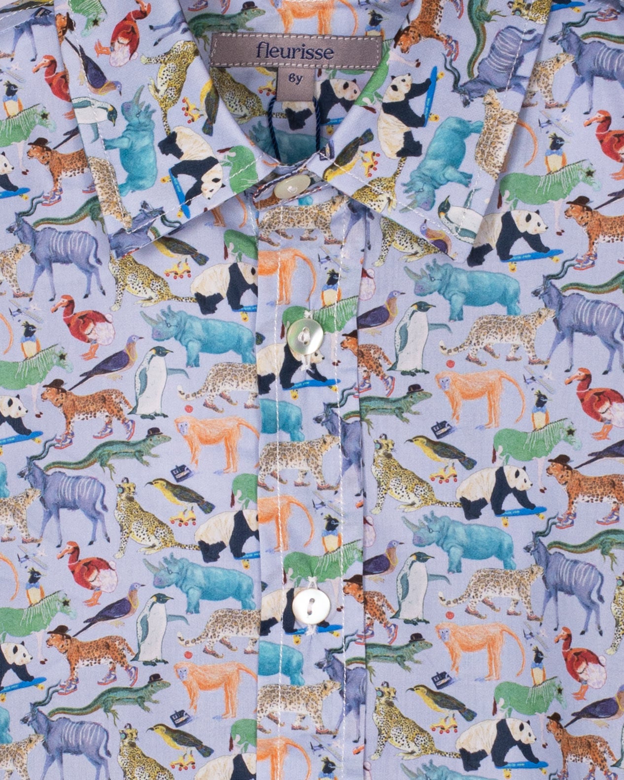 A long-sleeved boys’ button-down shirt made from Liberty of London cotton, featuring a detailed animal print in multicolor, shown hanging on a wooden hanger against a pale blue wall.