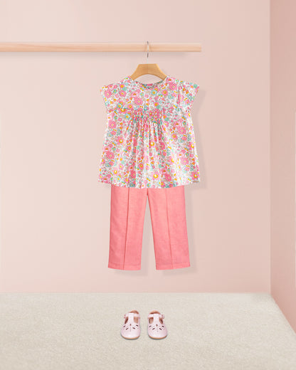 Floral top and pink pants with shoes on a light pink background