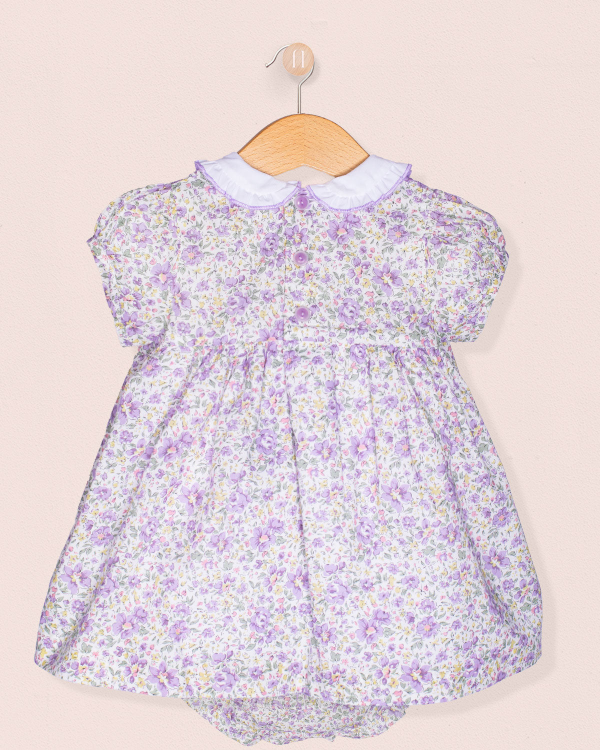 Floral baby dress on a wooden hanger against a beige background