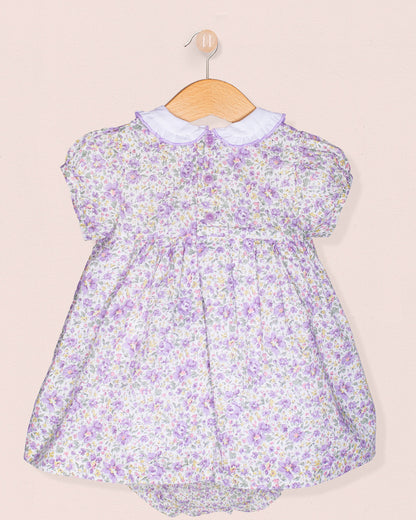 Floral baby dress on a wooden hanger against a beige background