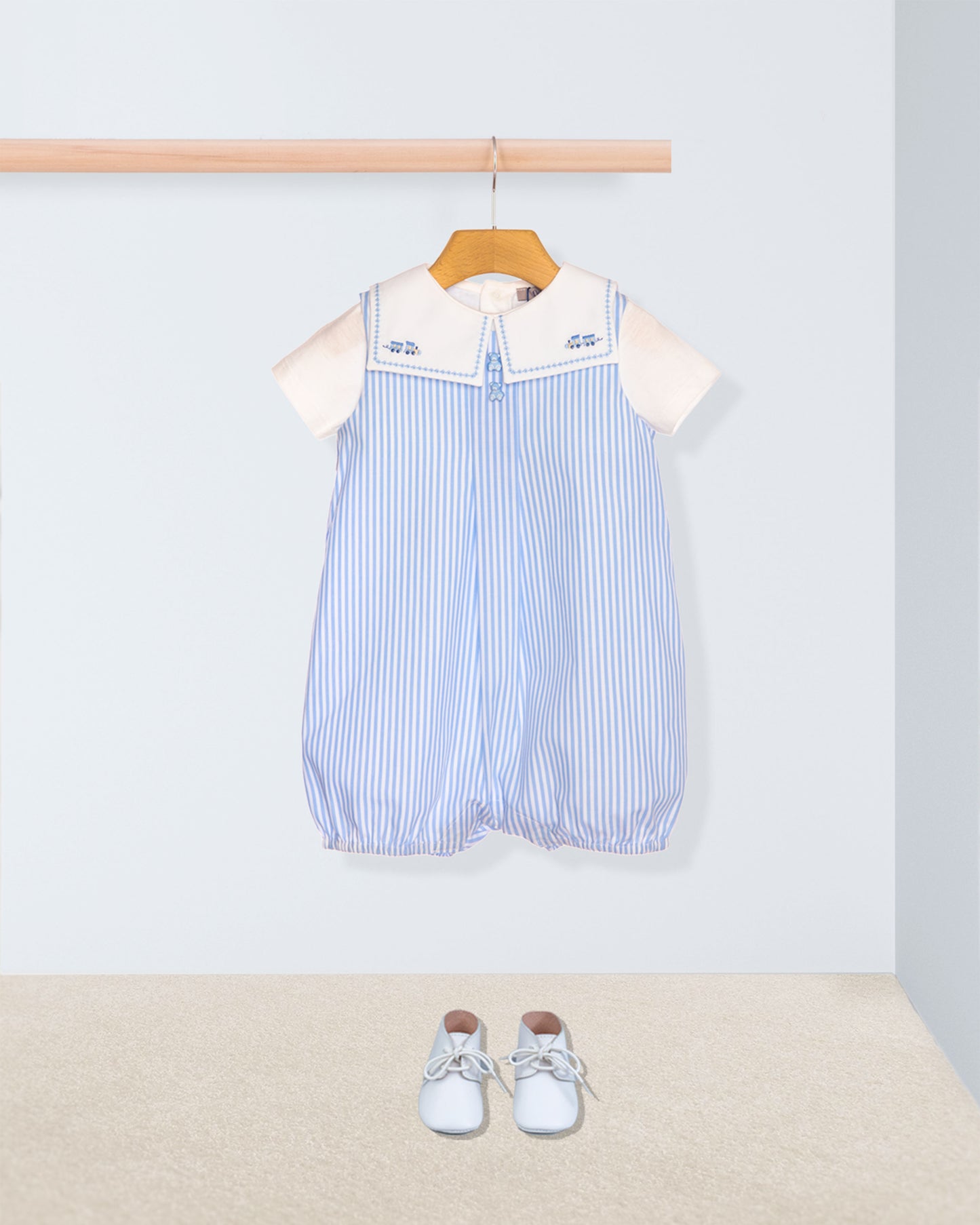 Baby romper with striped pattern and white collar on a hanger, with baby shoes on the floor.