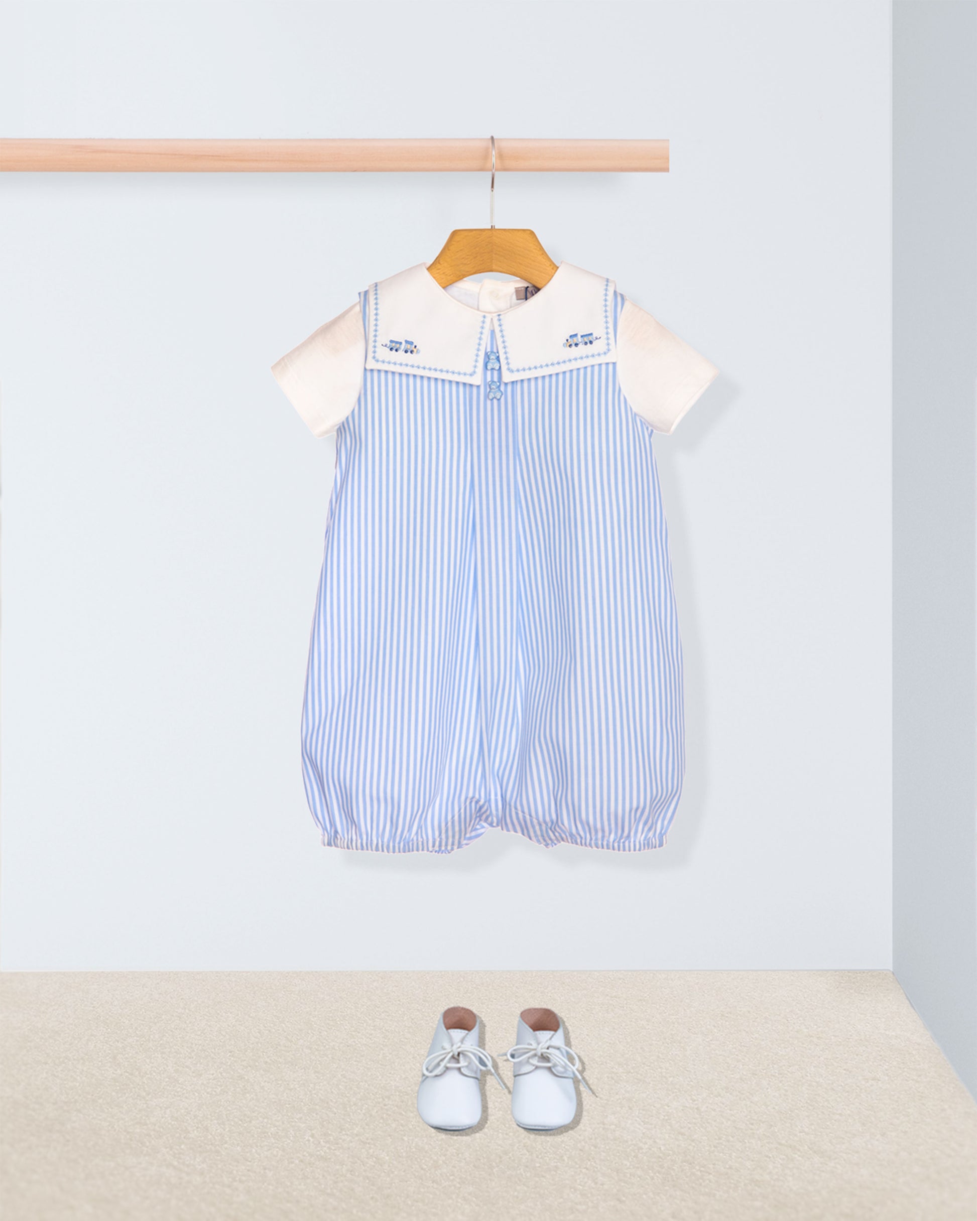 Baby romper with striped pattern and white collar on a hanger, with baby shoes on the floor.