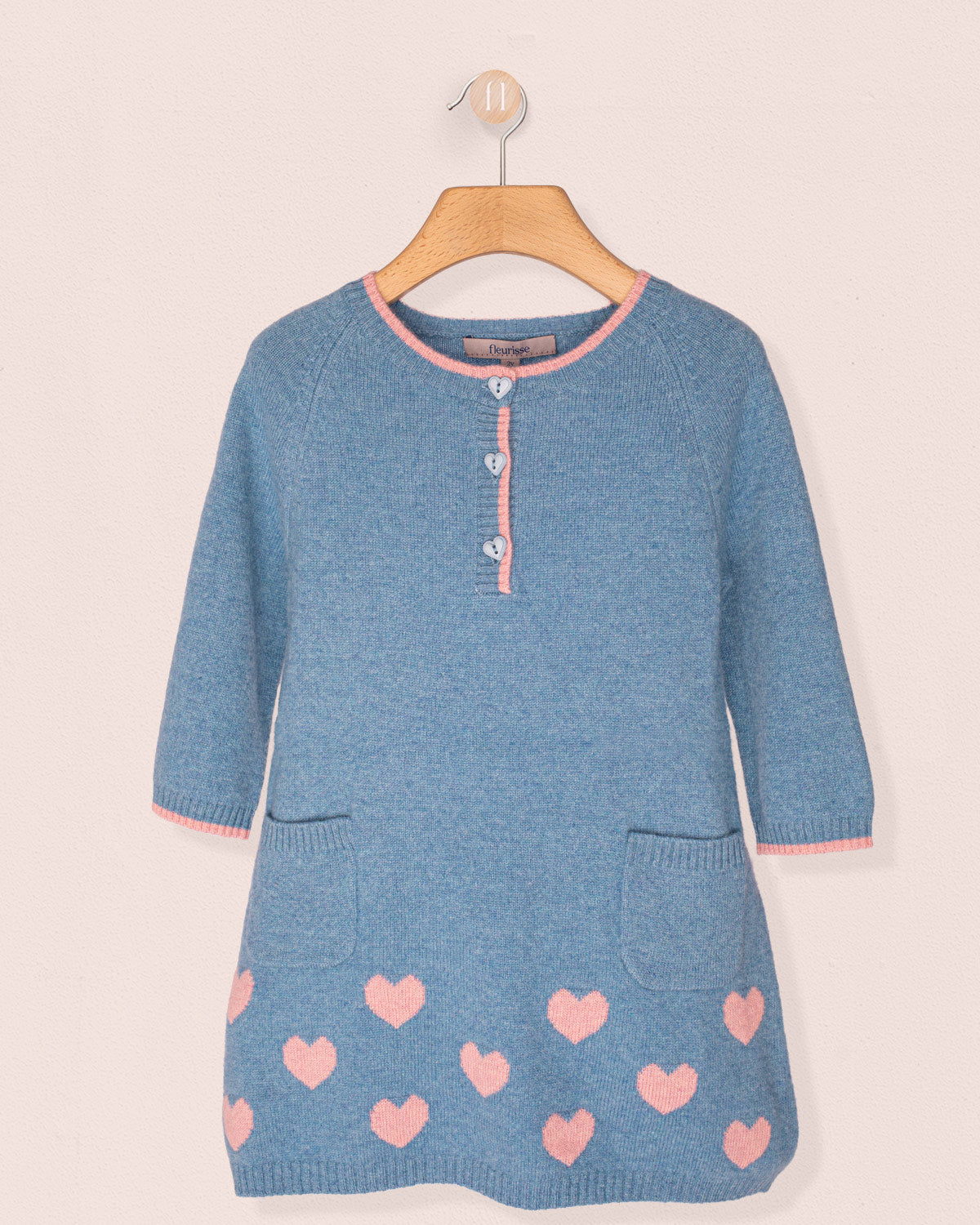 Blue knitted dress with pink heart patterns on a hanger against a light background