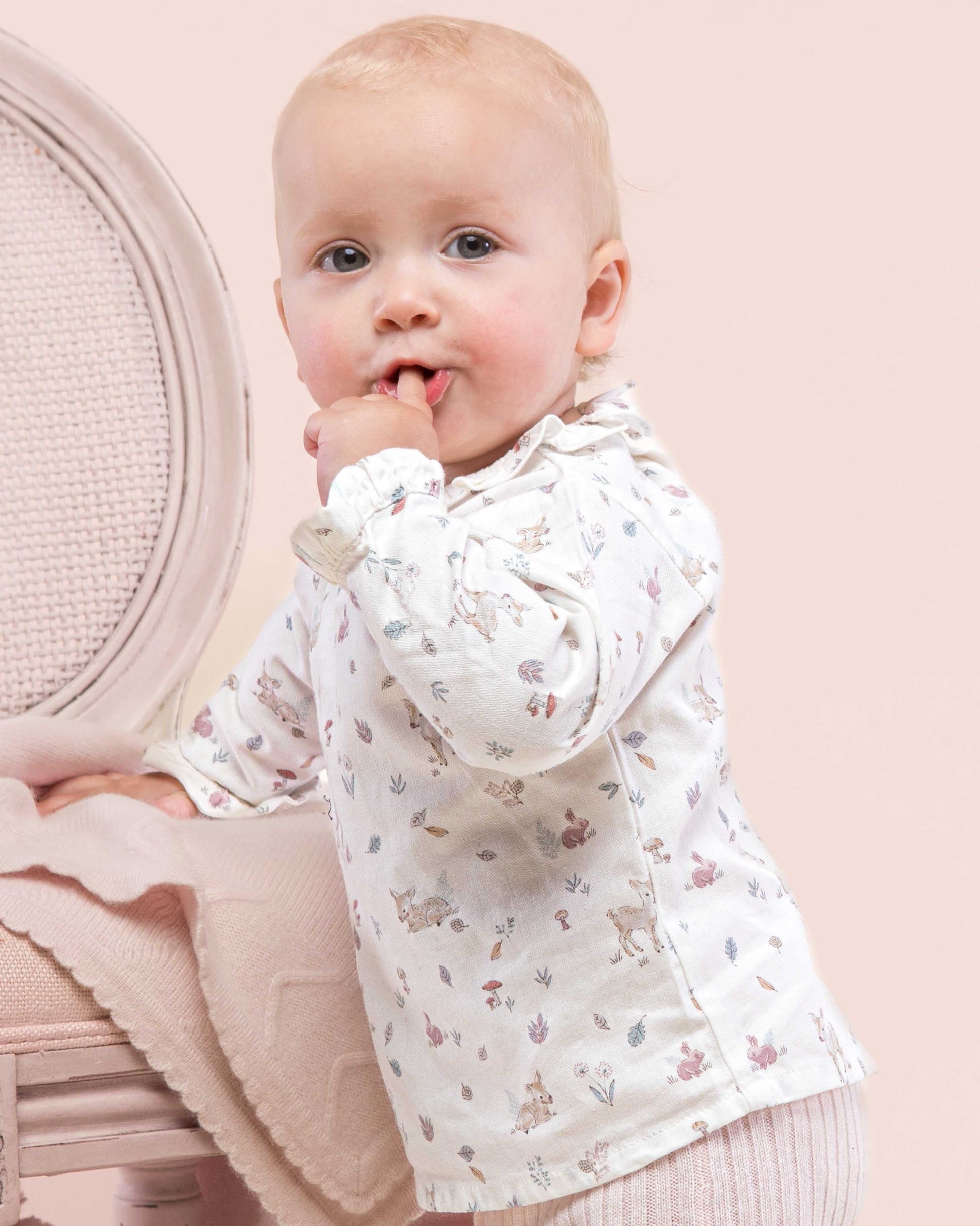 Baby model girl wearing Minette Pink Fawn Tunic facing to the side looking to the front showing the side of the tunic