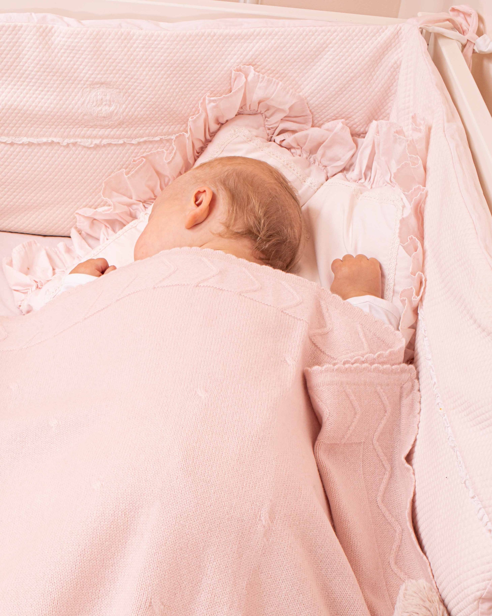 Baby sleeping on a crib with Cherie Cashmere Pink Blanket, showing the details and trimmings of the blanket