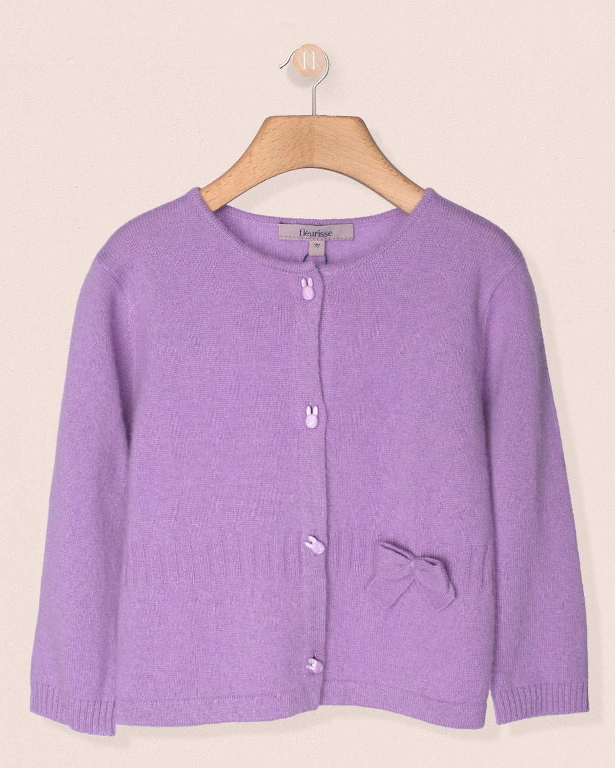 Purple cardigan on a wooden hanger against a beige background