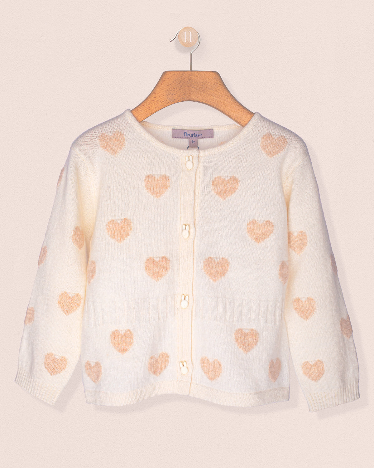 White cardigan with pink heart patterns on a wooden hanger against a light background