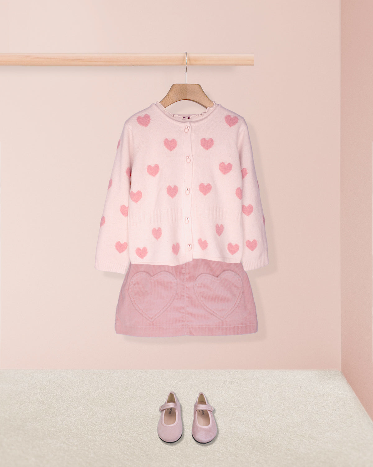 pink hearts cardigan on hanger with pink skirt and pink shoes on pink background