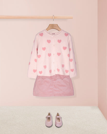 pink hearts cardigan on hanger with pink skirt and pink shoes on pink background