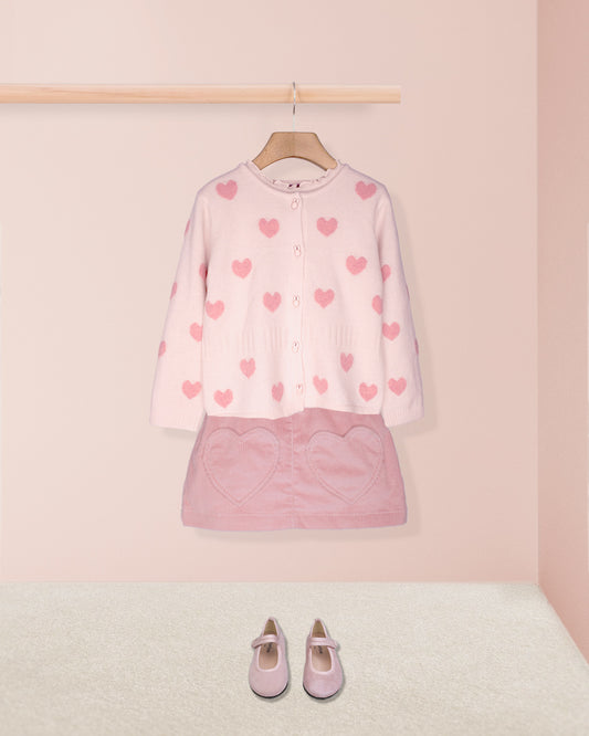 pink hearts cardigan on hanger with pink skirt and pink shoes on pink background