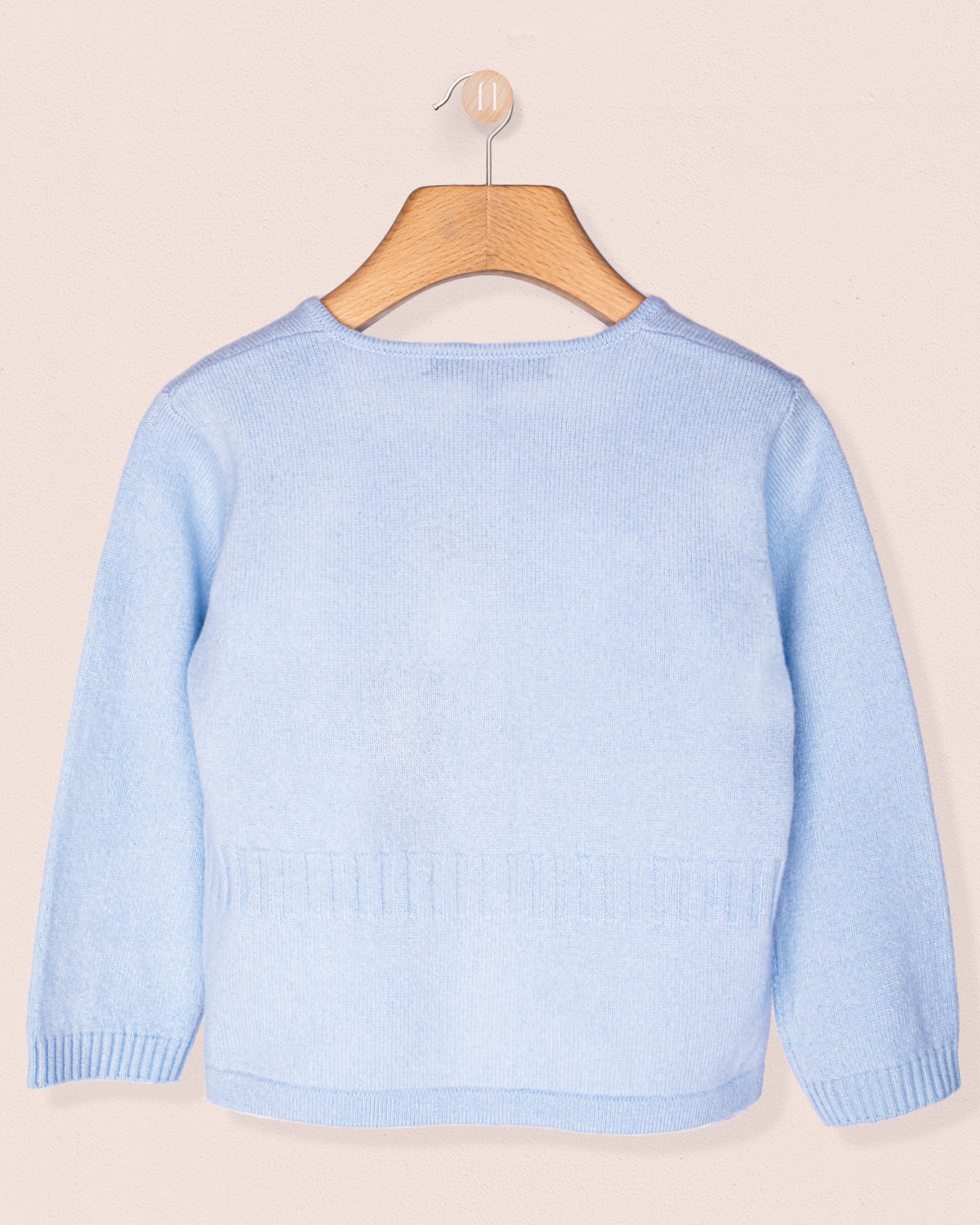 Back of a Light blue cardigan with a bow and bunny buttons, on a wooden hanger against a beige background
