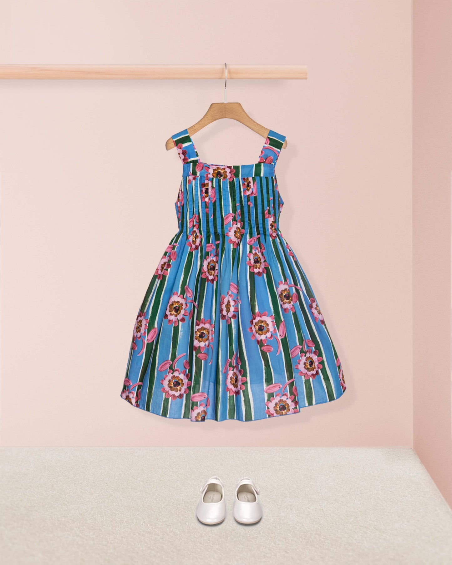 Blue floral dress on a hanger against a pink wall with white shoes on the floor.