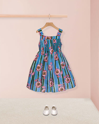 Blue floral dress on a hanger against a pink wall with white shoes on the floor.
