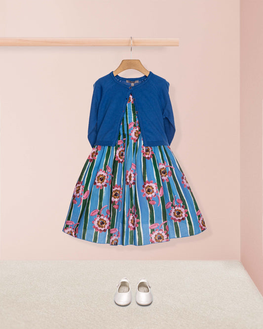 Blue dress with floral pattern and blue cardigan on a hanger against a pink wall.