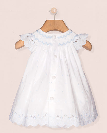 White baby dress with blue embroidery on a pink background