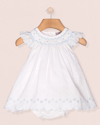 White dress with blue embroidery on a wooden hanger against a beige background