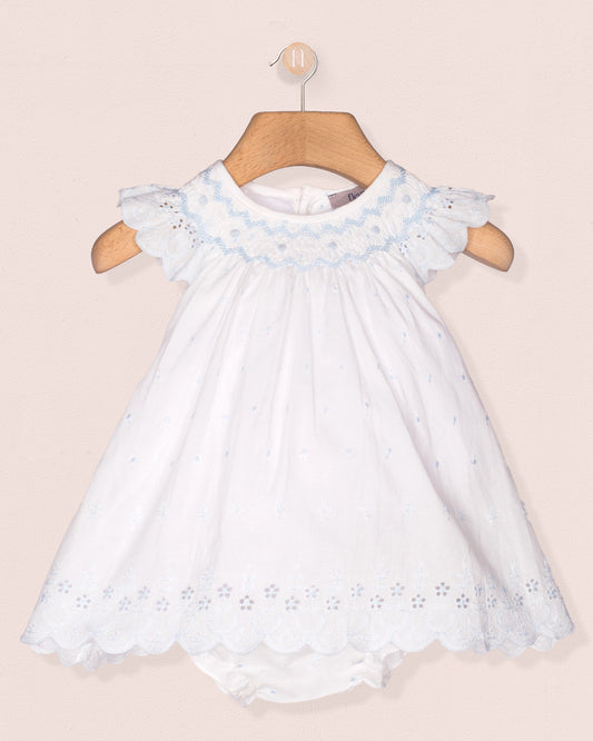 White dress with blue embroidery on a wooden hanger against a beige background