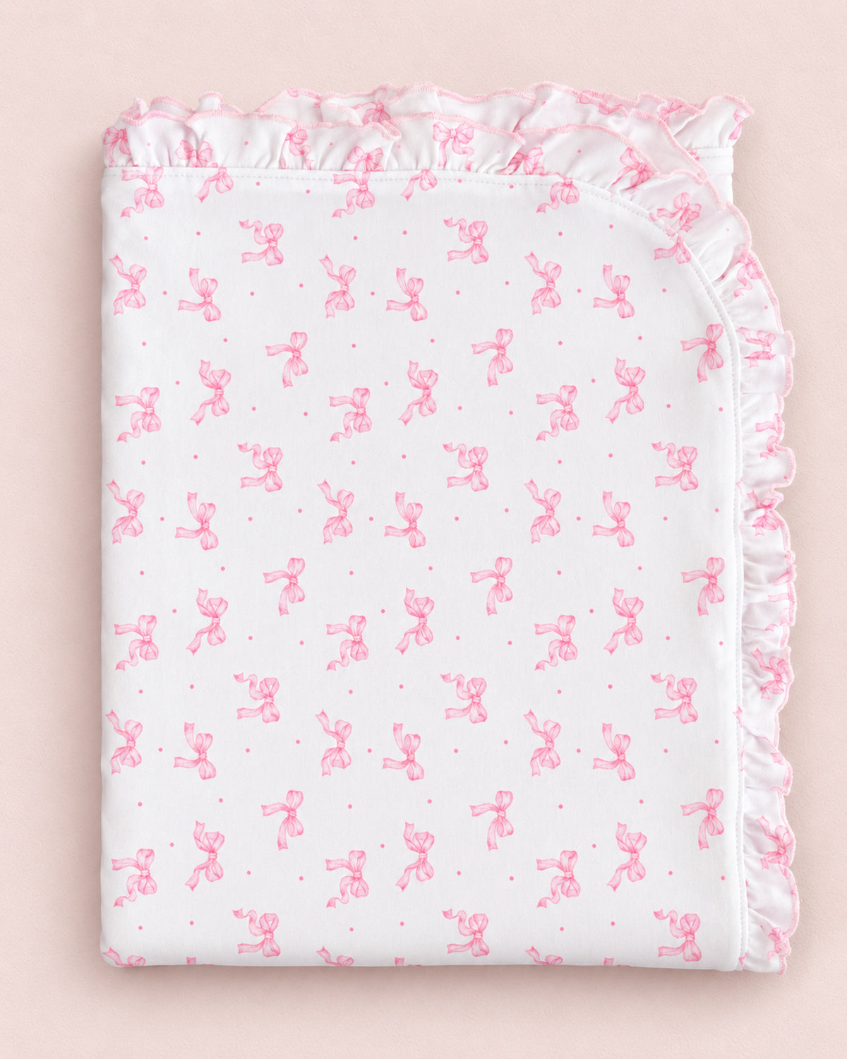 A folded white baby blanket or sheet featuring a repeating pink bunny pattern and a ruffled border, displayed on a soft pink background.