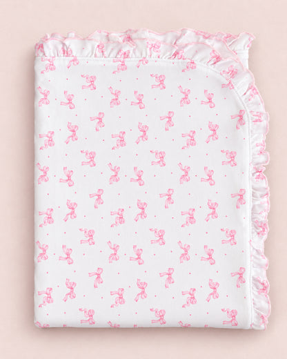 A folded white baby blanket or sheet featuring a repeating pink bunny pattern and a ruffled border, displayed on a soft pink background.
