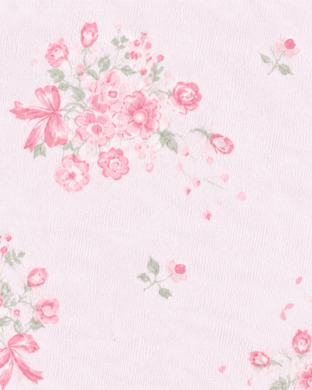 A close-up of a light pink textured fabric featuring a delicate floral print with pink roses, green leaves, and pink ribbon bows.