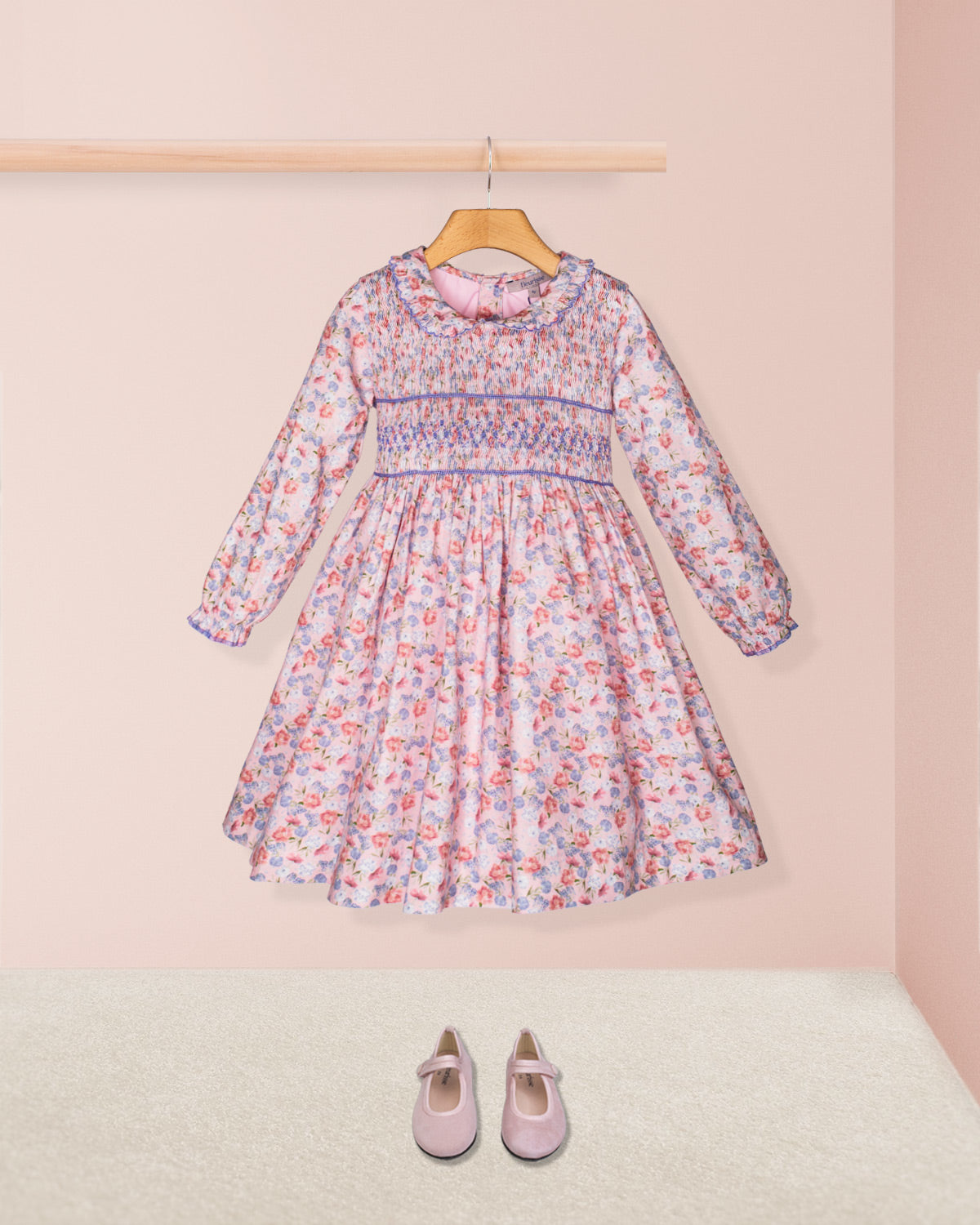 Floral dress on a hanger with matching shoes on the floor against a pink background