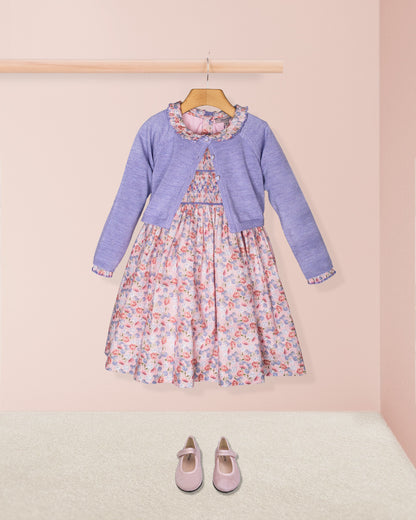 Children's outfit with floral dress and purple cardigan on a pink background