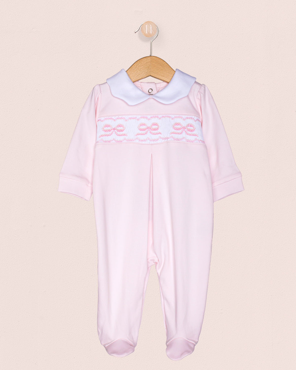 Pink baby romper with white collar and smocked bows  on a beige background
