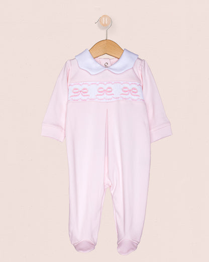 Pink baby romper with white collar and smocked bows  on a beige background