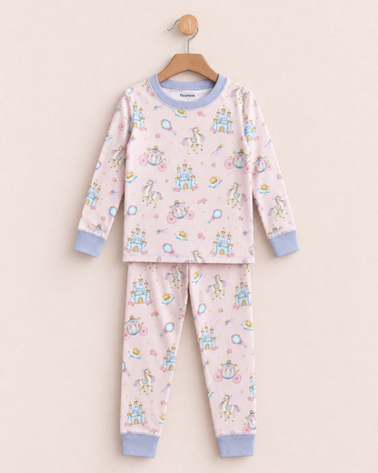 A two-piece children's pajama set hanging on a wooden hanger against a light beige background. The set features a long-sleeve top and matching pants in a pale pink color, decorated with a whimsical print of unicorns, castles, and bicycles in pastel blue, yellow, and green.