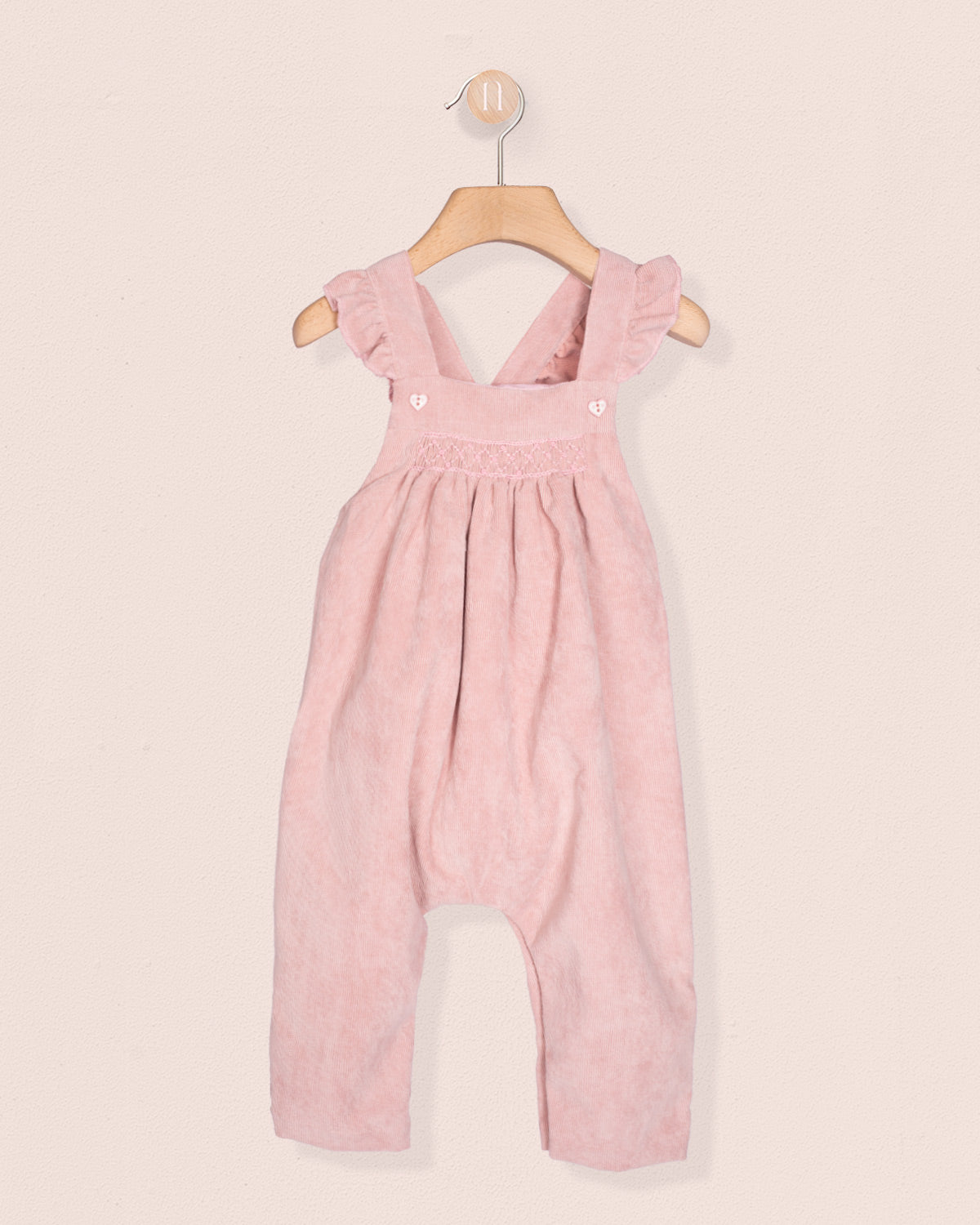 Pink children's overalls on a hanger against a light pink background