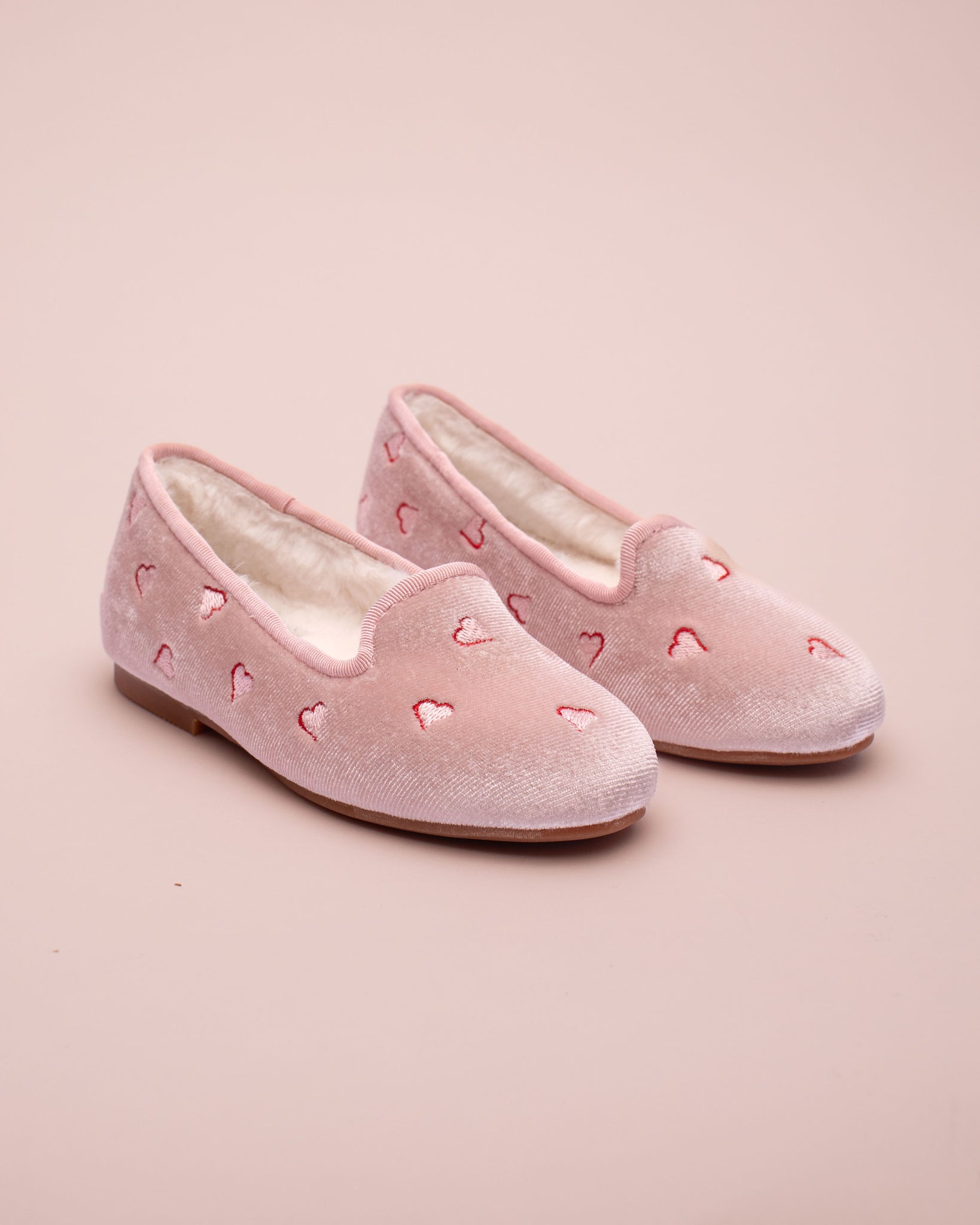 Pair of pink slippers with heart designs on a pink background