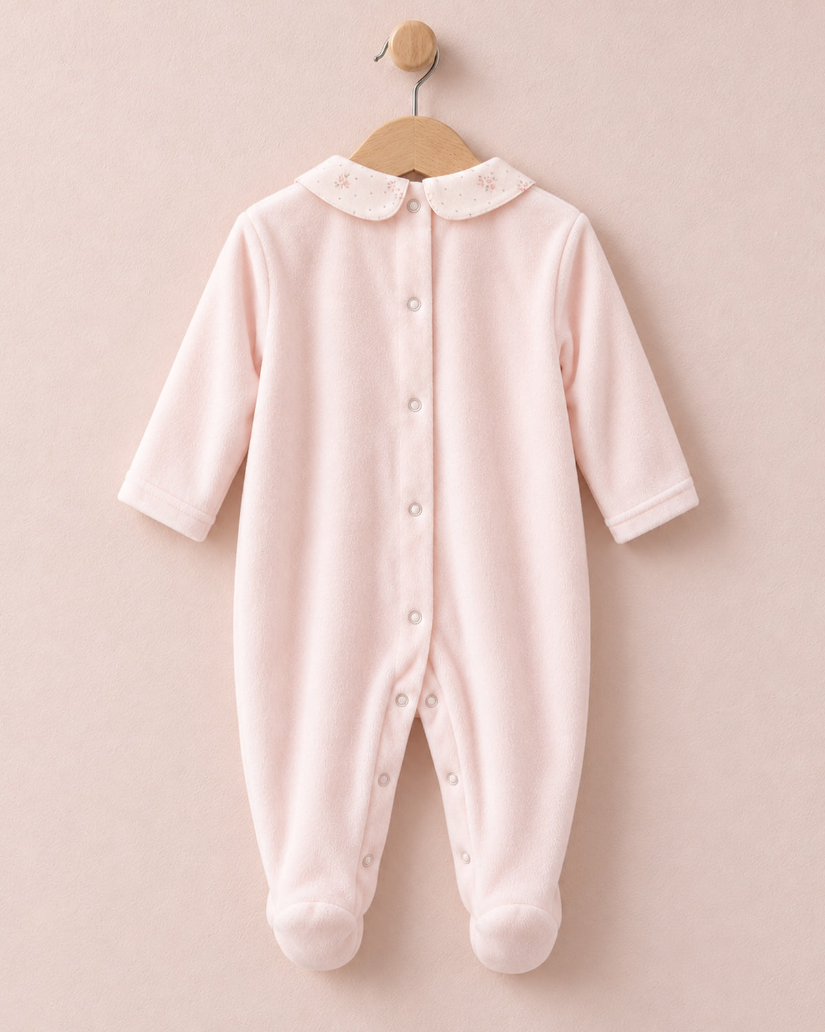 Back of pink velour baby onesie hanging from wooden hanger, with light pink floral motif collars.