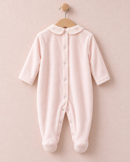 Back of pink velour baby onesie hanging from wooden hanger, with light pink floral motif collars.