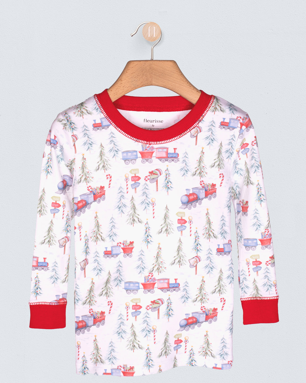 Children's long-sleeve shirt with train and Christmas tree pattern on a hanger against a light gray background.