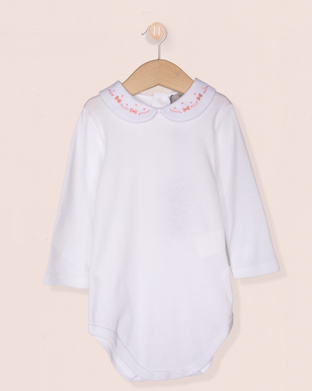 White baby dress with pink trim on a beige background