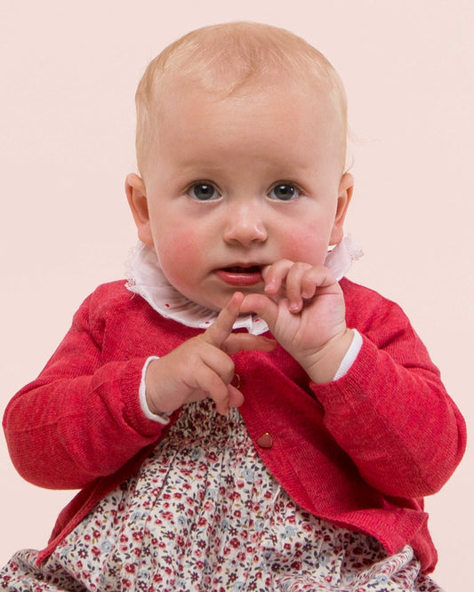 Baby girl wearing Serena Red Melange Cardigan fiddling with her fingers- showing the front of the sweater with one button closed